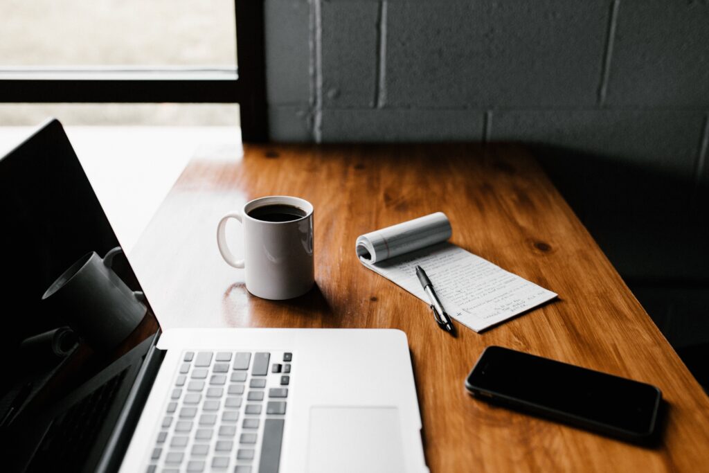 Laptop, Kaffeetasse und handschriftliche Notizen auf einem Holzschreibtisch